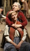 Mother Courage in red coat and looking off to the left behind Kattrin has her arms around the daughter's shoulder, Kattrin in Bohemian peasant dress and red vest looks off to the right, her hands dangling in her lap